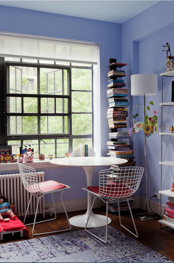 a pretty periwinkle space with a catchy window, a shelving unit, a white tale and wire chairs, a stack of books