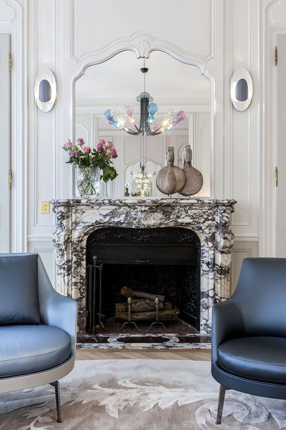 a refined living room with a black cast iron fireplace and a white marble mantel, blue and grey chairs, a mirror over it
