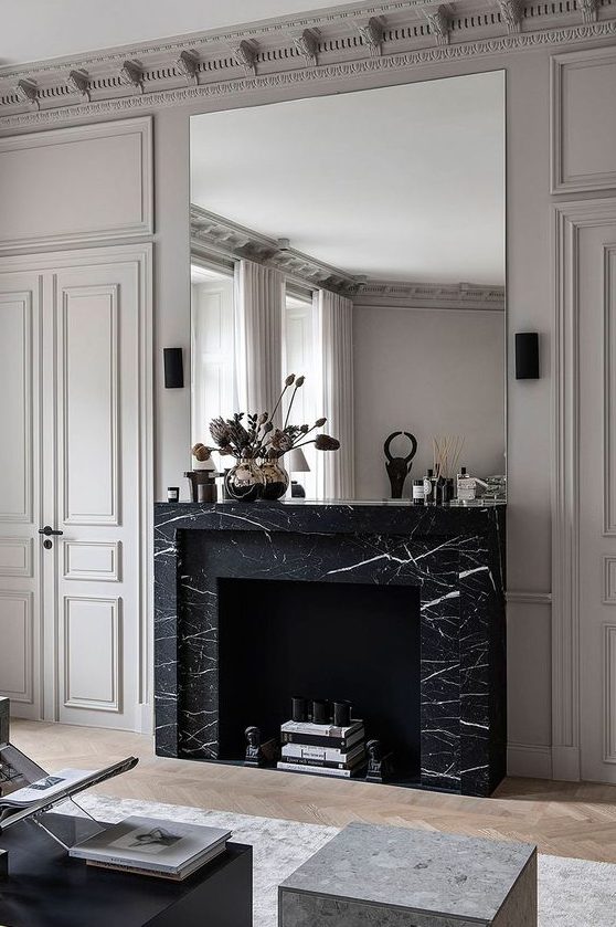 a refined monochromatic living room with a non-working fireplace clad with black marble and an oversized mirror over it