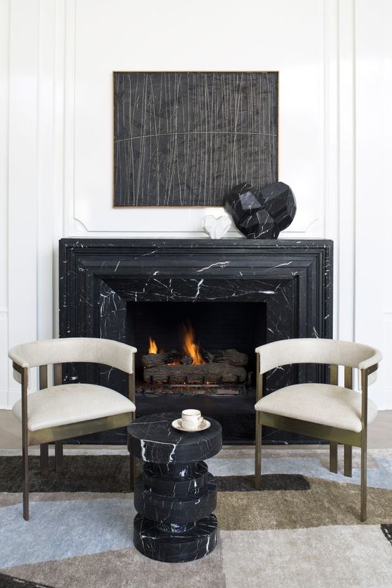 a refined nook with a black marble fireplace and a matching side table, gorgeous brass and velvet chairs
