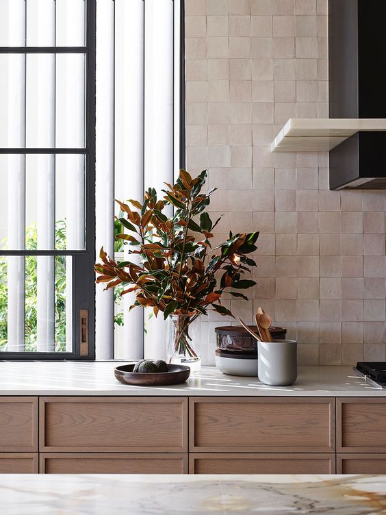 a refined stained kitchen with white countertops, a black hood, a blush zellige tile backsplash for a textural touch