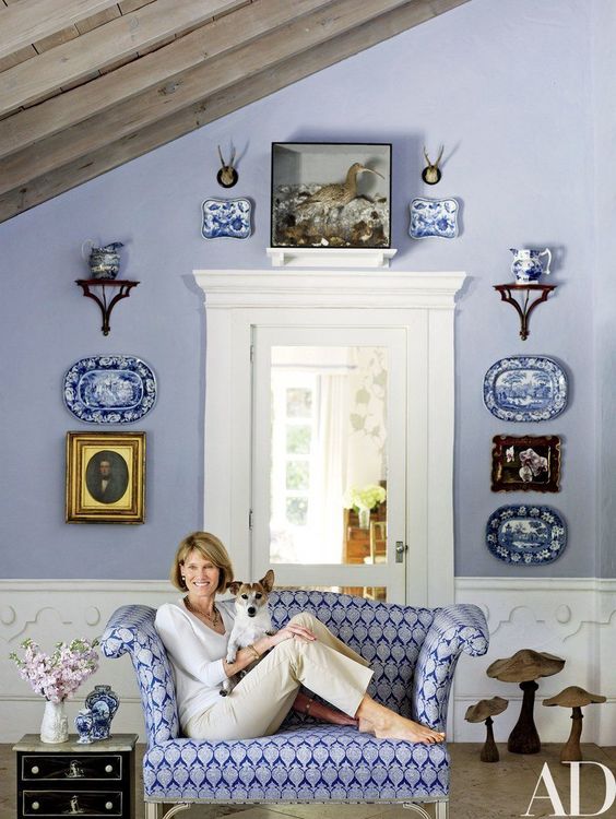 a refined vintage periwinkle space with white wainscoting, a gallery wall of plates and artworks and a printed very peri loveseat