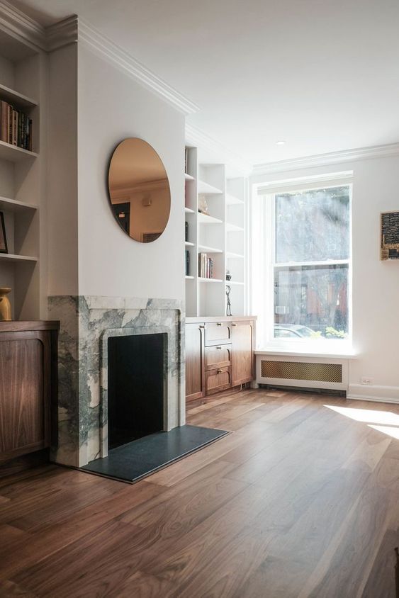 a sophisticated modern living room with white walls, rich-stained built-in furniture that matches floors, a fireplace clad with white marble