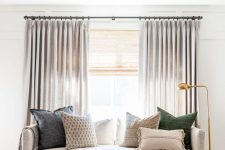 a stylish coastal bedroom done in neutrals, with woven shades and dove grey draperies – together they block out the light and match the color scheme