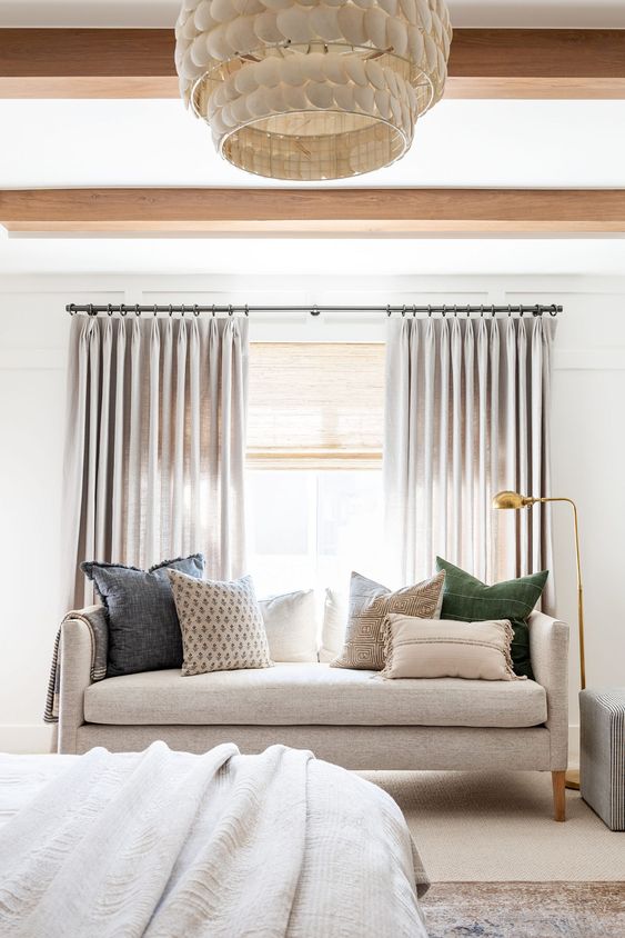 a stylish coastal bedroom done in neutrals, with woven shades and dove grey draperies   together they block out the light and match the color scheme