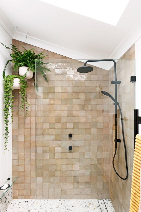 an attic shower space clad with blush and tan zellige tiles, with suspended potted plants and black fixtures for a modern feel