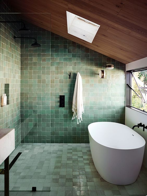 an eye-catchy attic bathroom completely done with green zellige tiles, with a skylight and a window plus black fixtures for a modern feel