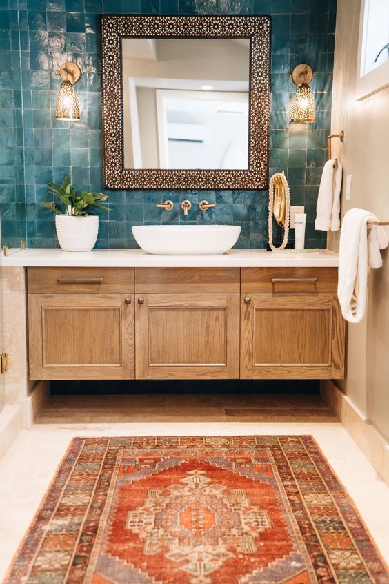 an eye catchy bathroom with a catchy teal zellige tile wall, a stained vanity, a rounded sink and a mirror in an ornated frame