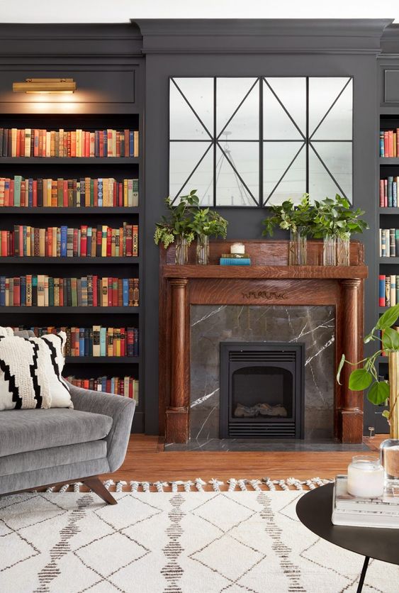 an elegant modern living room with graphite grey walls, built-in bookshelves, a fireplace clad with black marble and a TV hidden behind panels