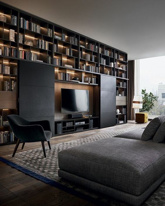 an elegant and refined black and grey living room with a huge lit up shelving unit on the wall and a TV hidden with sliding black panels