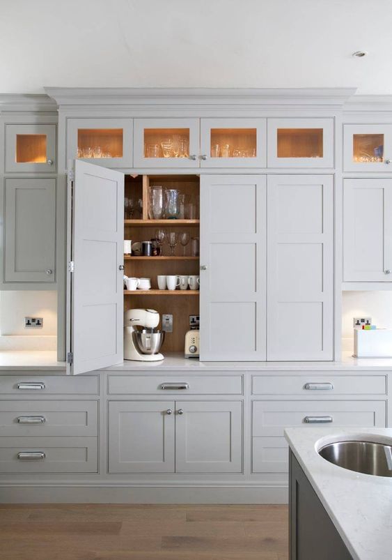 a dove grey contemporary kitchen with small appliances hidden in a cabinet with bi-fold doors to make the look sleek