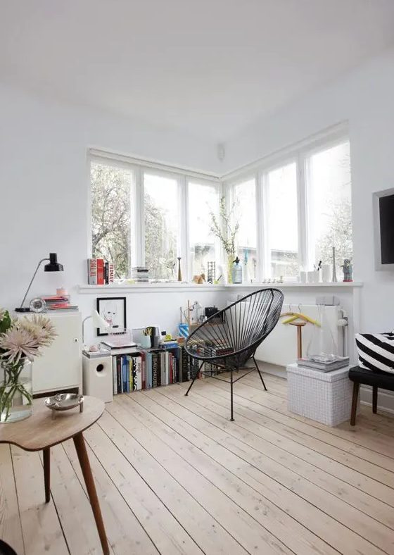 a lovely Nordic nook with a corner window, a windowsill used for storage, a black chair and a bookshelf is a very cozy corner