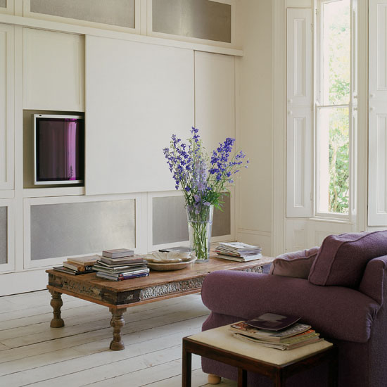 Large modern white living room with white washed floorboards, purple sofa, windows with shutters, plasma TV screen hidden by a canvas screen, wooden coffee table. Sim used H&amp;G 09/2004 p45.