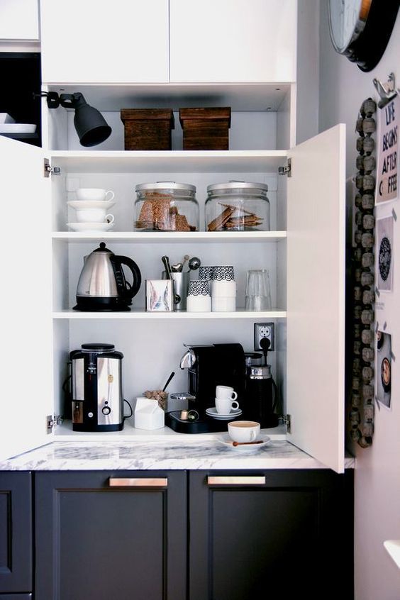 a home tea and coffee bar with all the necessary appliances and various cups and cookies hidden inside a kitchen cabinet