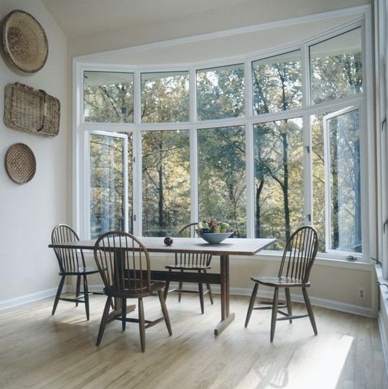 a farmhouse dining zone by a large bow window, with a vintage table and chairs plus decorative baskets on the wall