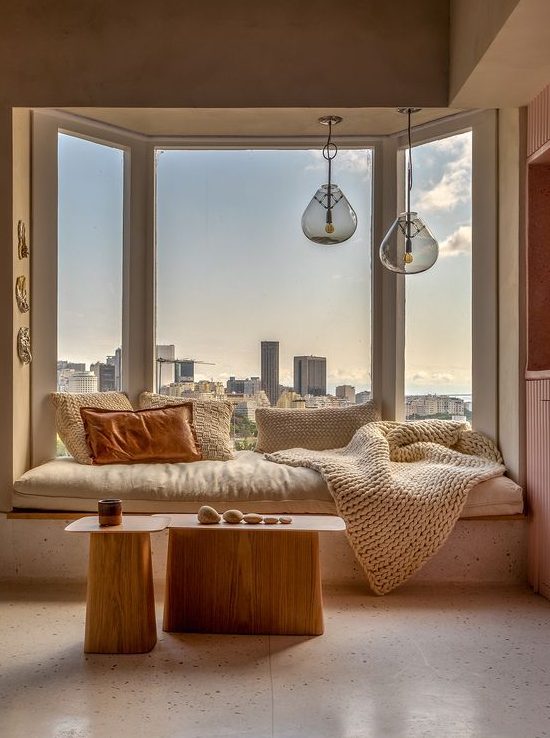 a lovely bow window with a windowsill daybed and pillows, pendant lamps over the bed and a duo of tables