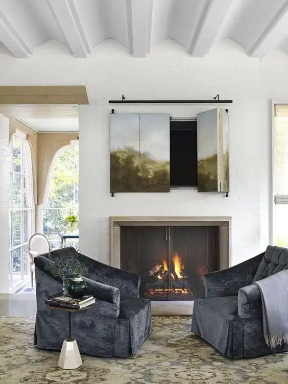 a cozy sitting nook with a real fireplace with a metal screen and a TV hidden behind an artwork that can be folded to watch TV