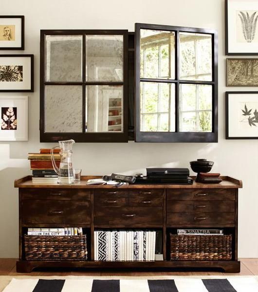 a dark stained storage unit with baskets and a TV hidden behind mirror framed doors not to break the harmony of the space