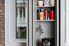 12 a small and narrow kitchen cabinet turned into a home coffee bar with a coffee maker on a retractable shelf and with lots of mugs