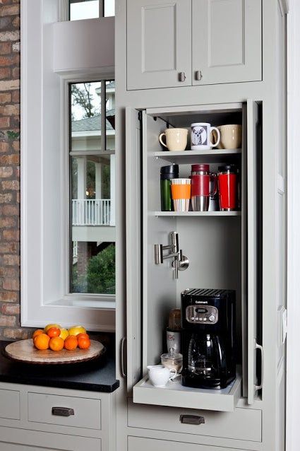 a small and narrow kitchen cabinet turned into a home coffee bar with a coffee maker on a retractable shelf and with lots of mugs