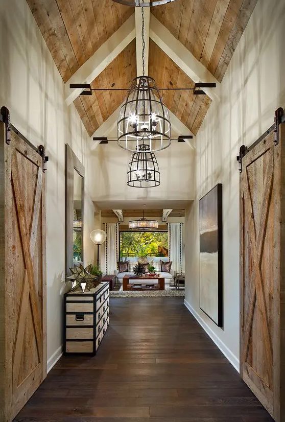 a farmhouse space with a dark-stained wooden floor, a light-stained ceiling and sliding doors plus elegant furniture, art and pendant lamps
