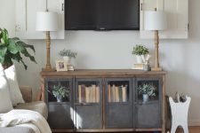 16 a neutral farmhouse living room with neutral sitting furniture, a TV on the wall hidden behind white barn doors and a metal and wood storage unit