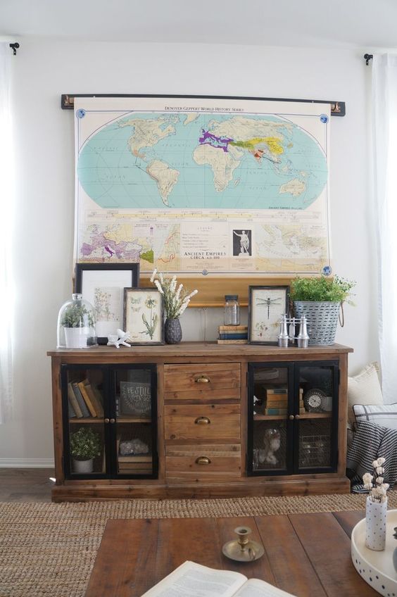 a stylish farmhouse space with a reclaimed wood storage unit, greenery, artwork and a large world map that hides the TV easily and effortlessly