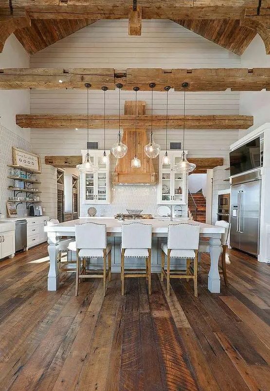 a white farmhouse kitchen with white cabinets, a refined kitchen island, a reclaimed wooden floor, light-stained wooden beams and a ceiling