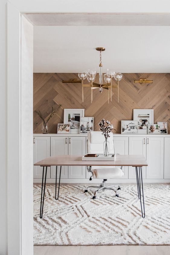 a beautiful home office with a rustic feel, with a herringbone clad statement wall, white shaker style cabinets, a hairpin leg desk and a cool chandelier