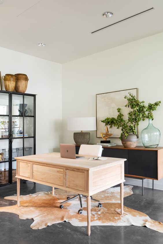 a whimsical and eye-catchy home office wiht a black storage unit and a glass buffet, a stained desk and a cowhide rug