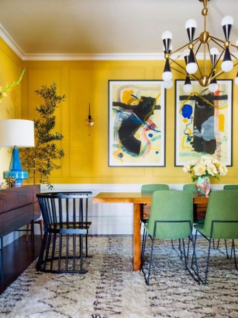 a colorful dining room with bold yellow walls, a stained table and credenza, green chairs and an elegant chandelier