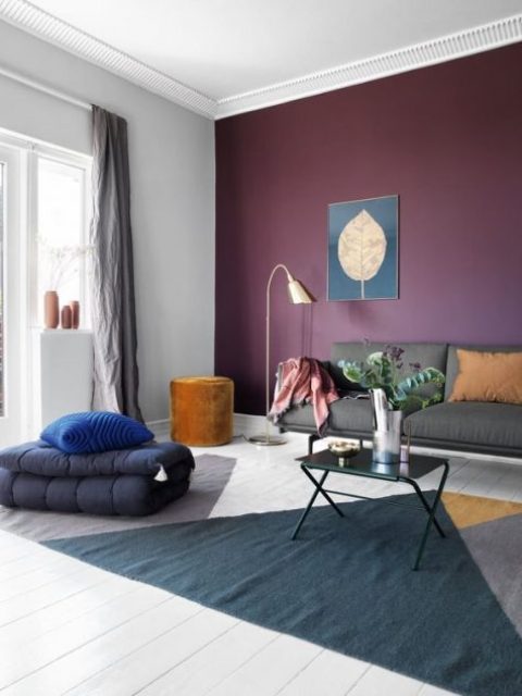 a bold living room with an eggplant accent wall, grey furniture, a bold color block rug and touches of gold