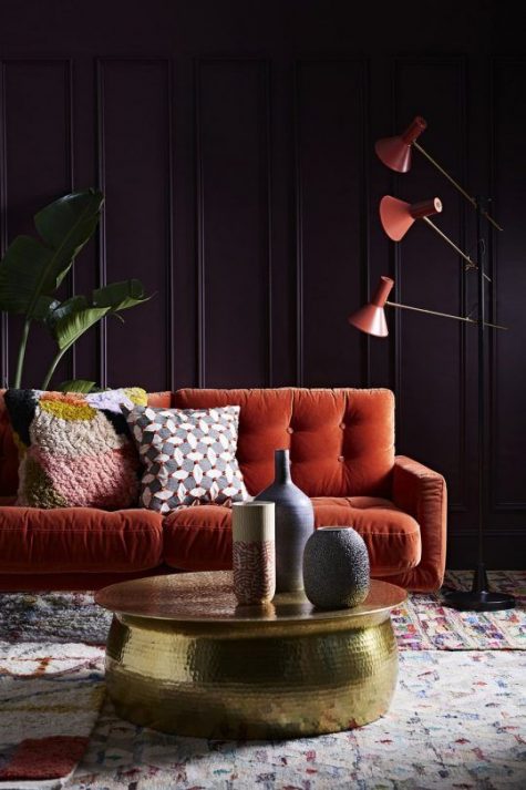 a fantastic living room with deep aubergine walls, an orange sofa and lamps and a gold hammered table