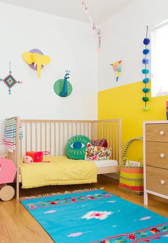 a modern colorful kid's room with a color block yellow and white wall, bright bedding and a rug, cardboard taxidermy and accessories