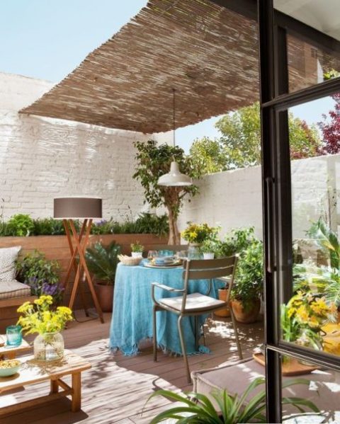 a small and bright deck with simple outdoor furniture, a roof over the space, bright blooms and plants is a cool space