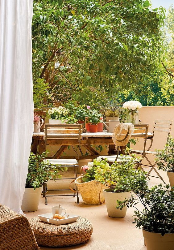 a beautiful Mediterranean terrace with a simple wooden dining table, potted plants and blooms, a jute pouf is very welcoming