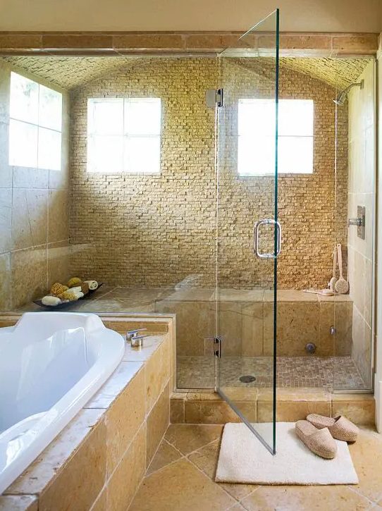 a beautiful warm-colored bathroom with a large shower space with glass doors and a bathtub clad with tiles