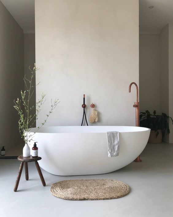 a beautiful contemporary spa bathroom with an oval tub, a dark-stained sotol, a jute rug and some greenery