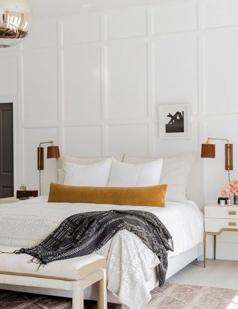 a sophisticated neutral bedroom with a creamy upholstered bed, an upholstered bench, leather sconces, white refined nightstands and paneled walls