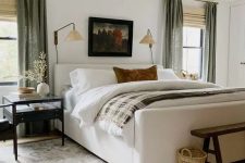 60 a chic and welcoming bedroom with a creamy upholstered bed, neutral bedding, chic nightstands, a wooden bench, baskets and green curtains