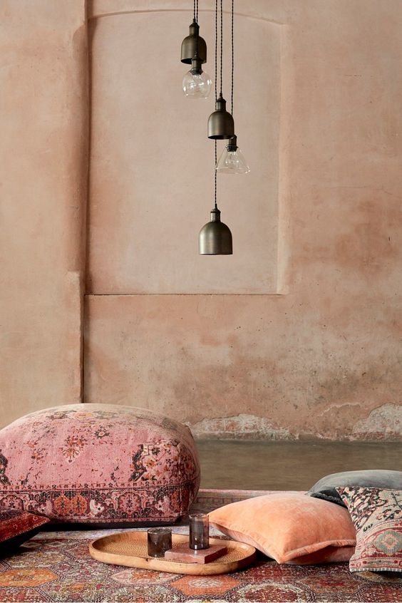 a Moroccan space with pink limewashed walls, dark pendant lamps, cushions and pillows on the rug on the floor