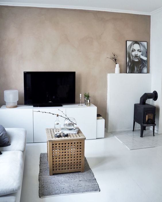 a Scandi living room with a mauve limewashed wall, white furniture, an IKEA Hol table and a black hearth in the corner
