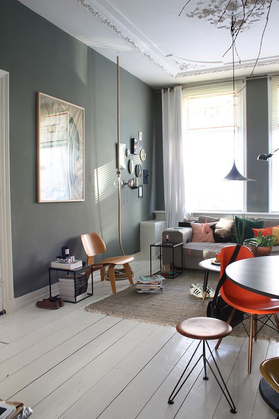 a Scandi living room with slate grey walls, a grey sofa, a black table and mismatching chairs, a small gallery wall and pendant lamps