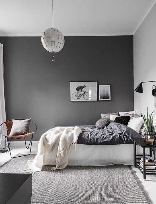 a Scandinavian bedroom with a slate grey accent wall, a white bed with lots of pillows, black sconces and a nightstand