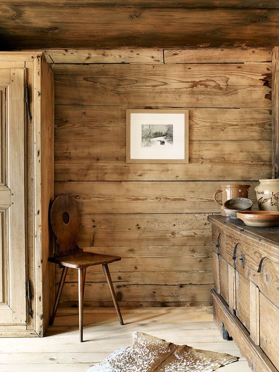 a beautiful chalet kitchen with rough wooden walls, a wooden storage unit and carved cabinets, a stained chair and vintage tableware