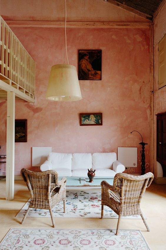 a beautiful living room with pink limewashed walls, a white sofa, woven chairs, a delicate table and a pendant lamp