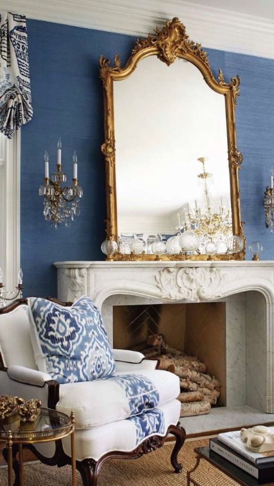 a bold and refined living room with blue grasscloth wallpaper, an antique fireplace, a mirror in an ornated frame, wall sconces and exquisite furniture