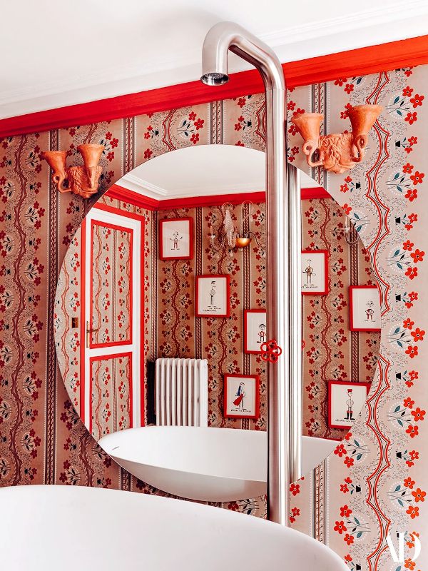a bold bathroom done with coquelicot printed wallpaper, an oval sink, a tube with a red fixture is gorgeous