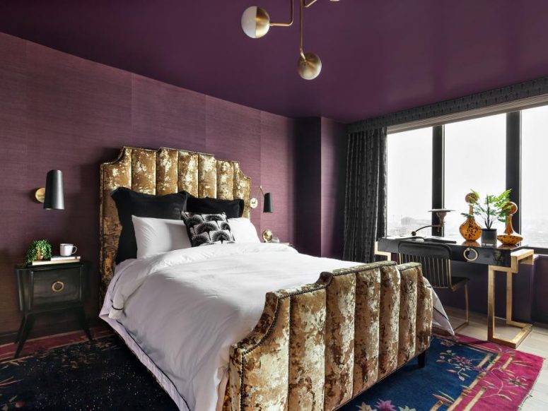 a bold refined bedroom with a purple ceiling and purple grasscloth wallpaper, a gold crushed velvet bed, black nightstands, gold touches