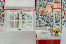 a bright bathroom with white subway tiles and marble hex ones, bold printed wallpaper, a coquelicot vanity and white and red shades